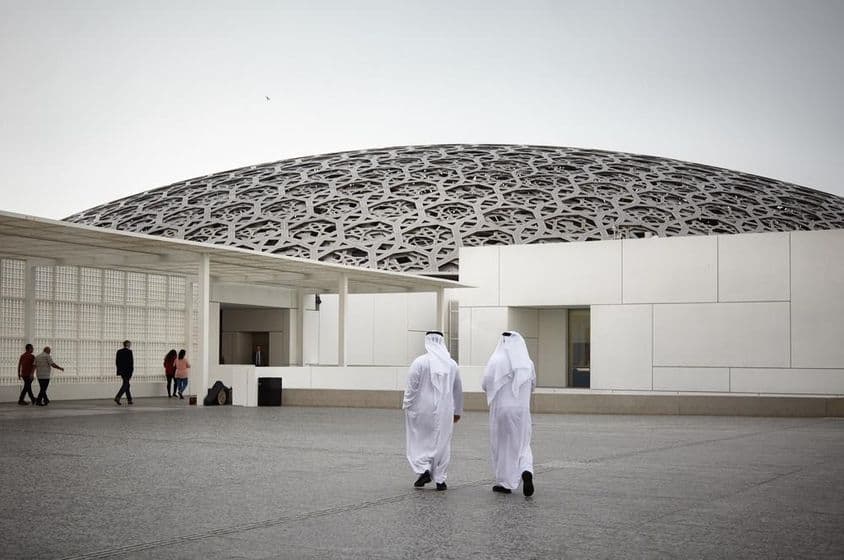 Az Abu Dhabi Louvre múzeumot látogató turisták és két emirates, fehér tradicionális ruhában.