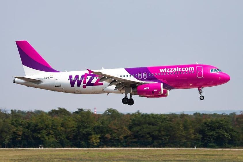 Wizz air repülő alacsony magasságban repül, háttérben egy erdő látható. 