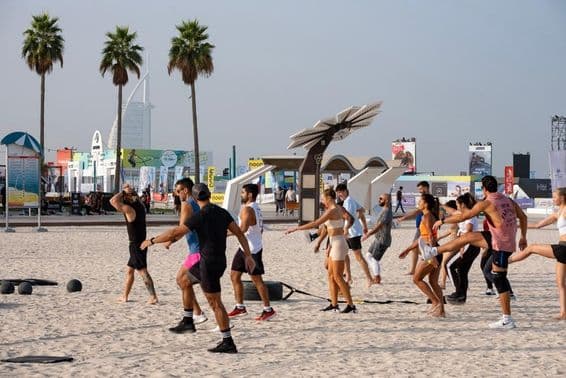 Egy csoport ember tornázik a Dubai Fitness Challenge keretében, homokos tengerparton. 