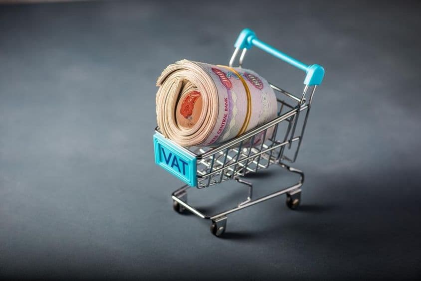 Kis bevásárlókocsi, benne köteg dirham, az elején a vat azaz adó szó.