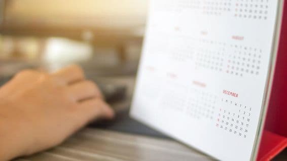 Egy kéz, mellette naptár látható pár hónap elmosódva, december jól olvasható.