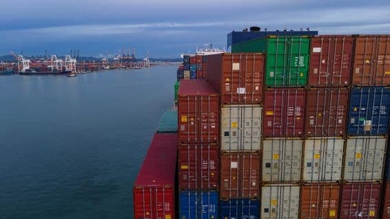 Bal oldalon egy tengeri kikötő öböl látható, jobbra egymásra pakolt konténerek.