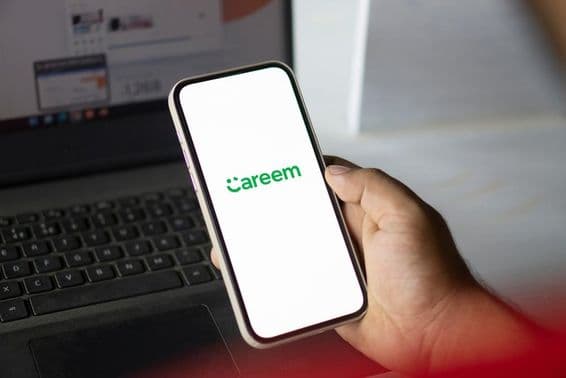 Egy telefon careem appot futtat amit egy kéz fog, a háttérben egy notebook látható.
