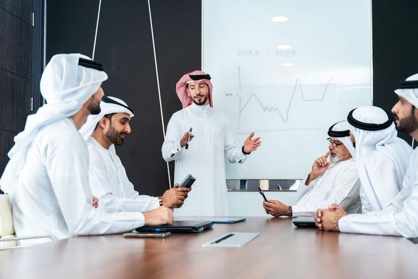 Arab tervezők beszélgetnek egy tábla előtt, asztalon egy notebook és telefon.
