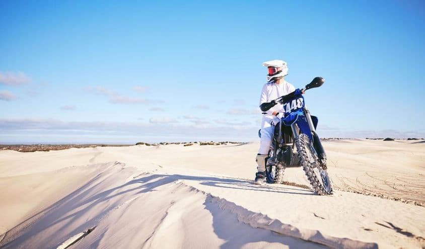 Sivatagba motorozó ember , fehér ruhában kék motoron.