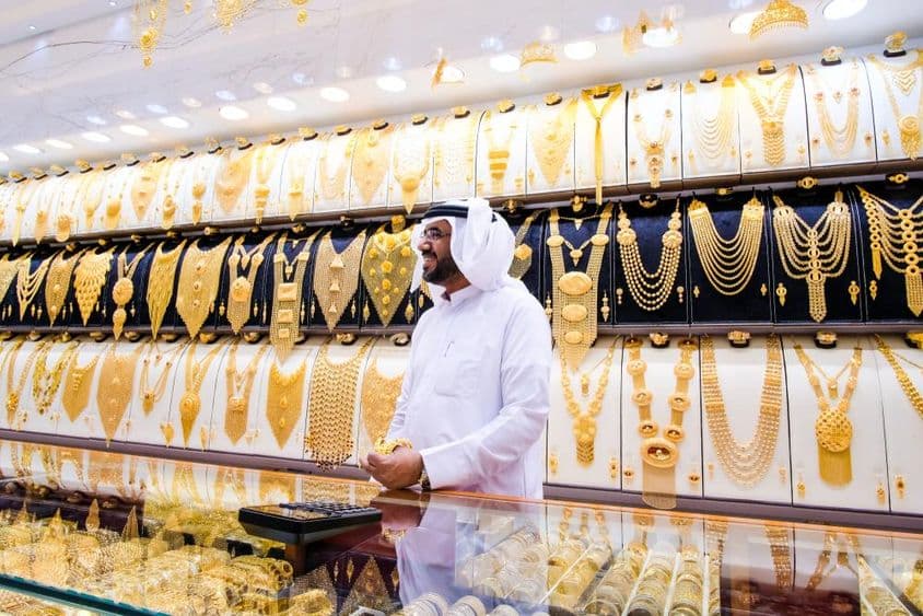 Dubai arany árus, háttérben sok arany nyakék, előtérben az árus tradicionális fehér ruhában.