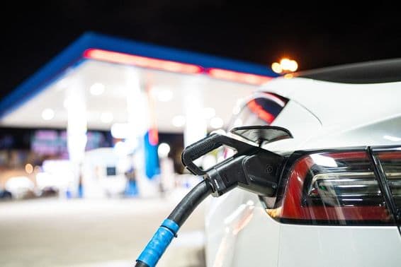 Egy teslát töltenek, egy benzinkút van a háttérben.