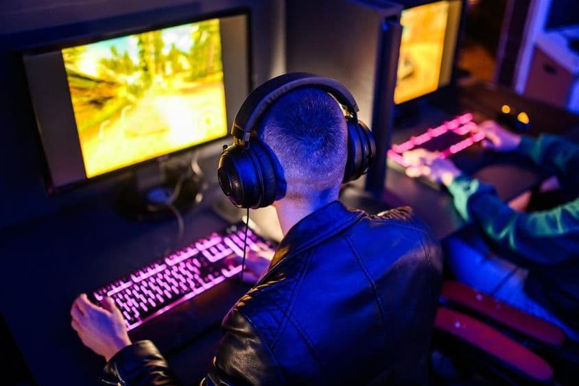 Online játékosokat látni, elötte világító billentyűzet és monitor.