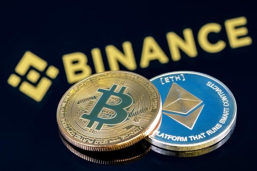 Binance felírat a háttérben a fekete asztalon egy bitcoin és egy etherium érme látható.