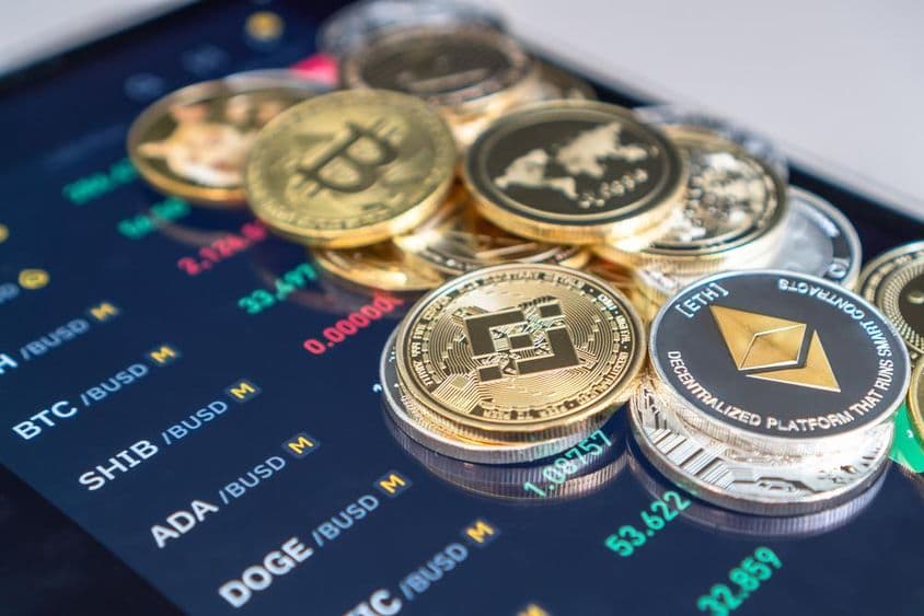 Eterium és bitcoint érmék vannak egy telefon előlapjára rakva amin a criptotozsde árai láthatóak.