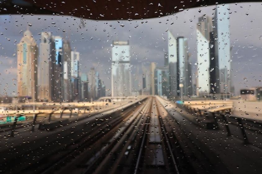Dubai metro ablakon látszik hogy esik az eső, a háttérben a felhőkarcolok látszanak.
