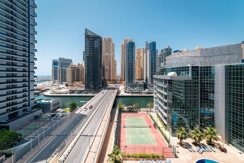 Egy teszinpálya látható Dubaiban mellette és mögötte felhőkarcolok, és vizen motorcsónak halad.