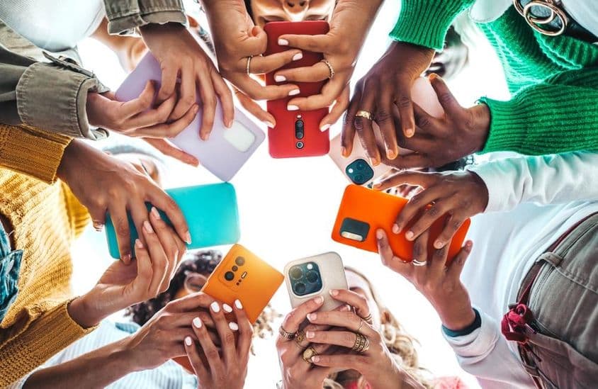 Emberek telefonnal a kezükbe körbe állnak alulról látszik a kezük.