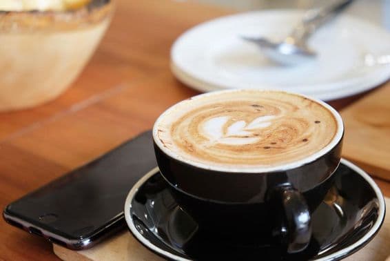 Egy pohár capuccinó van az asztalon mellette egy telefon.