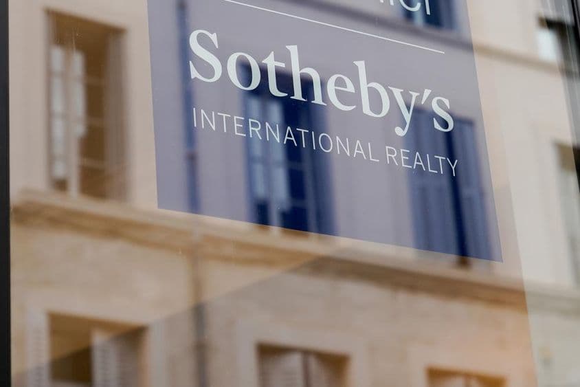 Sotheby’s felírat látható egy ház elején, átlátszó táblán.