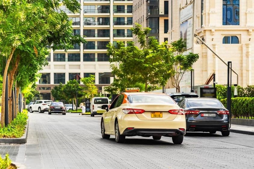 Dubai autók az úton, előtérben egy taxi, mögötte házak.