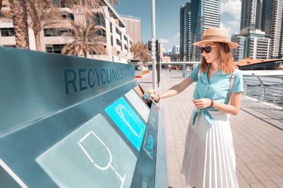 Dubai szelektív hulladékgyűjtőbe dobnak be egy flakont, háttérben felhő karcolok.