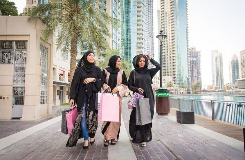 3 emirates hölgy vásárlás után, szatyrokkal megy, háttérben felhőkarcolok.
