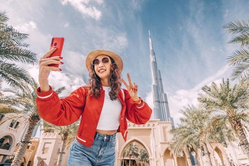 Fiatal nő, piros felsőbe szelfizik, Burj Khalifa látszik a háttérben.