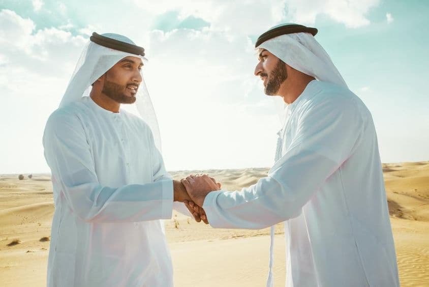 Két arab férfi kezet fog a sivatagban.