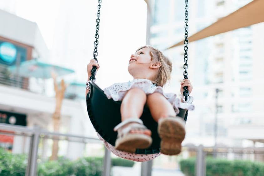 Boldog kislány hintázik az ovoda udvarán.