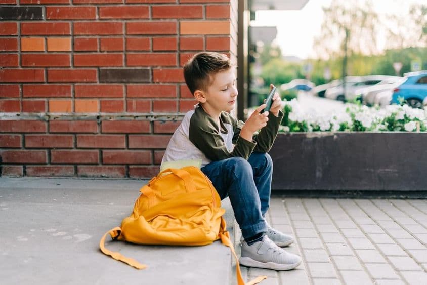 Kisfiú telefonozik az iskola lépcsőjén.