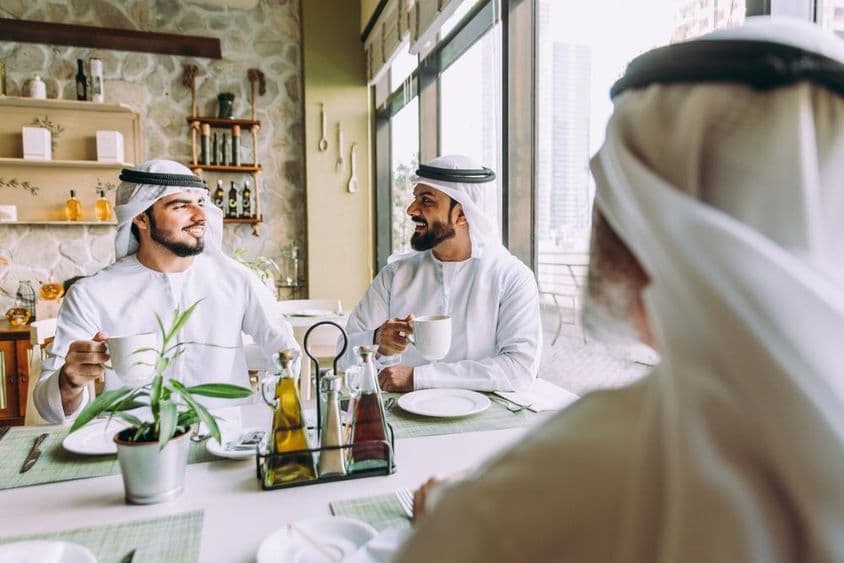 Három üzletember teázik Dubajban, hagyományos emirátusi ruhát viselve.