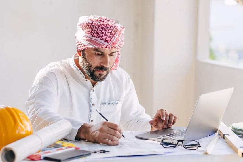 Arab építészmérnök, aki alaprajzon dolgozik.