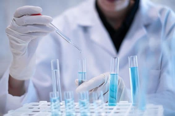 Tudós pipettázik kék folyadékot kémcsőbe laboratóriumban.