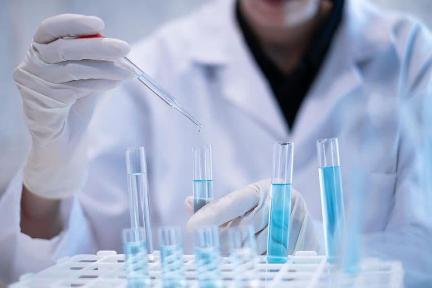 Tudós pipettázik kék folyadékot kémcsőbe laboratóriumban.