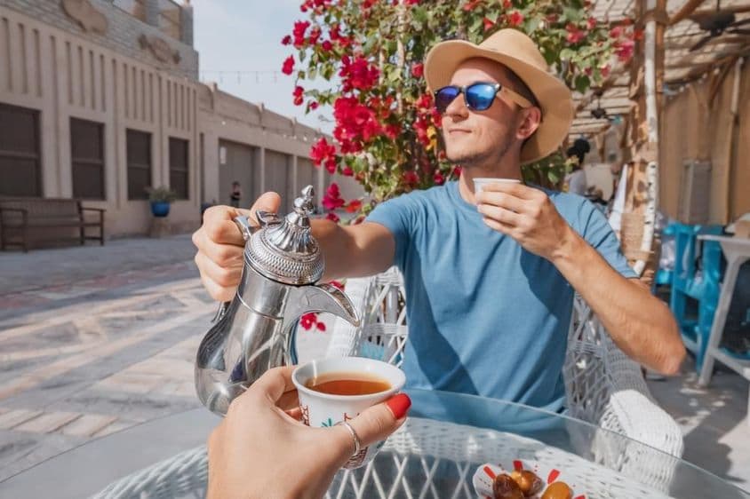 Egy férfi Dubajban egy  arab kávézóban piheni ki az utazását, és egy csésze aromás kávét tölt egy dallah kávéskannából.