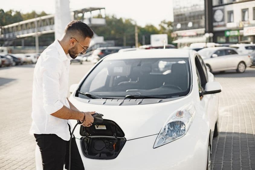 Arab fiatal férfi fehér elektromos autót tölt.