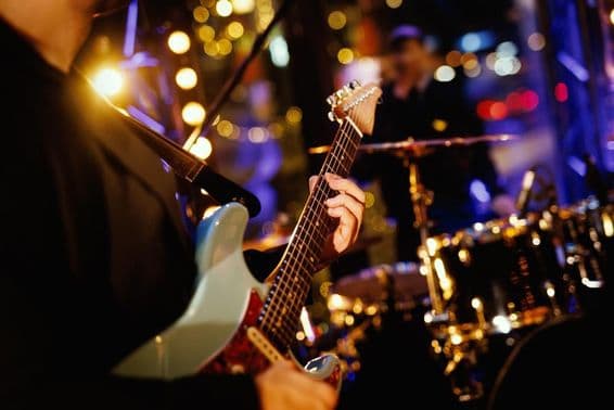Egy gitáros akkordot játszik le a fogólapon egy zenekar fellépése közben.