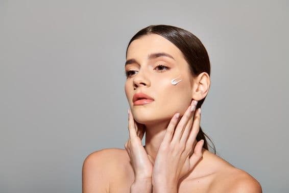 Egy barna hajú fiatal nő szépséget és öngondoskodást árasztó krémet ken az arcára.