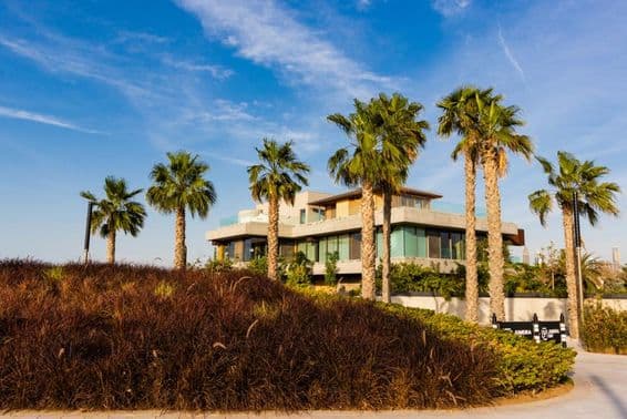 Dubai, pálmafákkal körülvett villa felhős háttéren naplemente előtt.