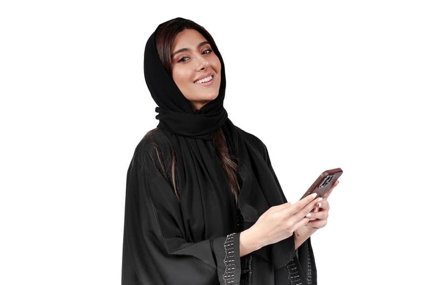 Arab abayat viselő emirátusi üzletasszony,  mobiltelefon használatával dolgozik.