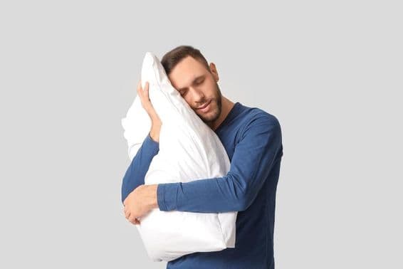 Fiatal férfi pizsamában, puha párnával.