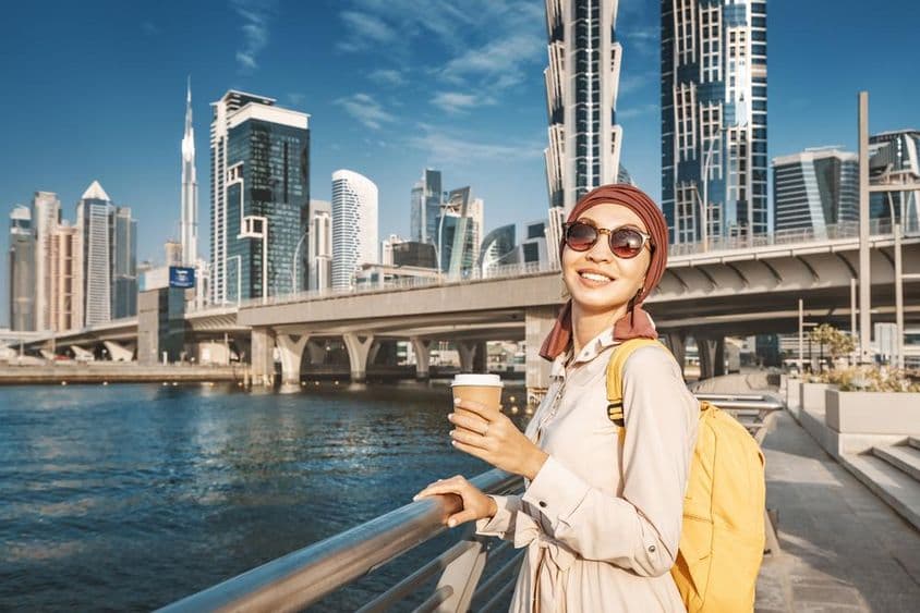 Muszlim nő sárga hátizsákkal sétál a Dubai-csatorna partján.