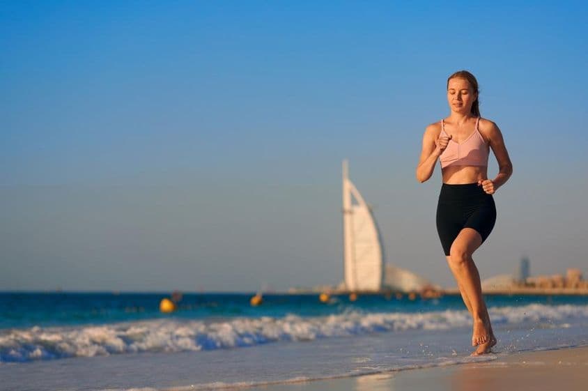 Fiatal nő fut a strandon Dubaiban háttérben Burj Al Arab Jumeirah.