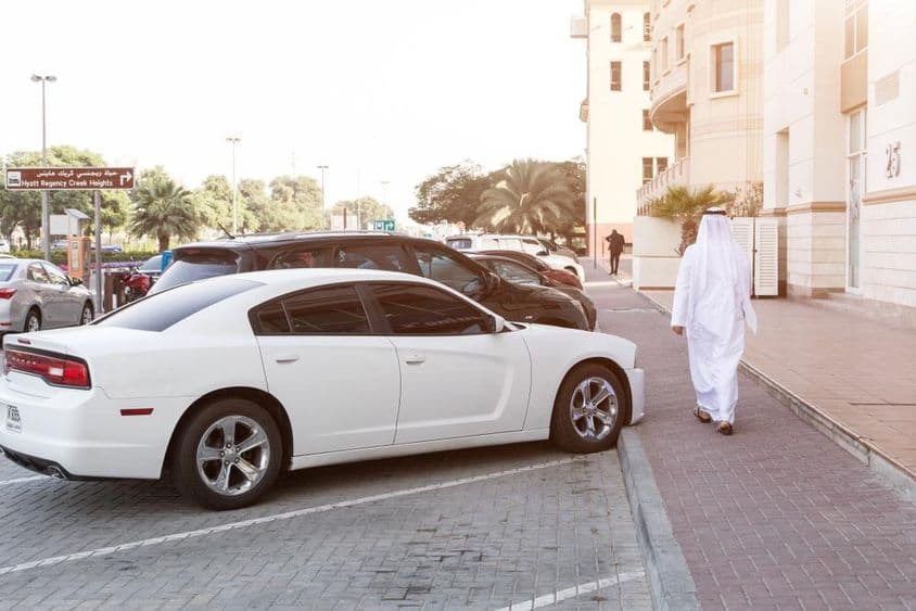 Dubai utcáin: Egy férfi nemzeti ruhában és egy fehér Dodge a parkolóban.