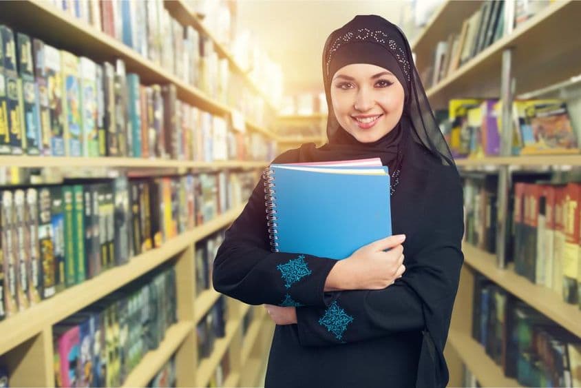 Arab diák áll a könyvtárban könyvekkel a karján.