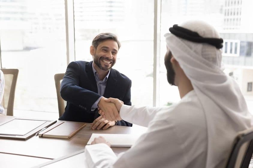 Vidám üzletember kezet fog arab partnerével.