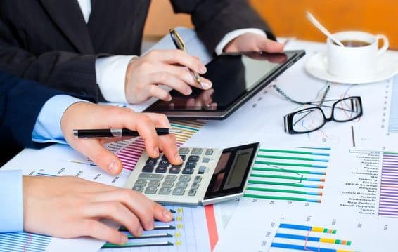 Grafikonok, számológép, tablet, szorgos kezek tanulmányozzák az értékeket.