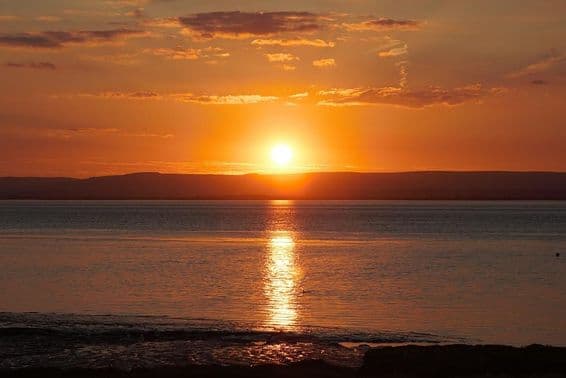 Lenyugvó nap tükröződik a vízen és a felhőkön a nyári napfordulón.
