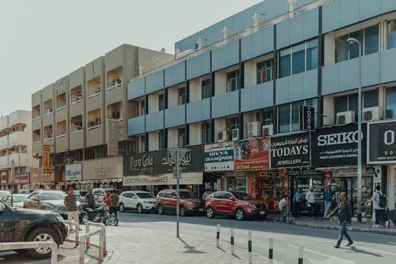 Forgalmas Bur Dubai utca ékszerüzletekkel, gyalogosokkal és autókkal egy napsütéses napon.
