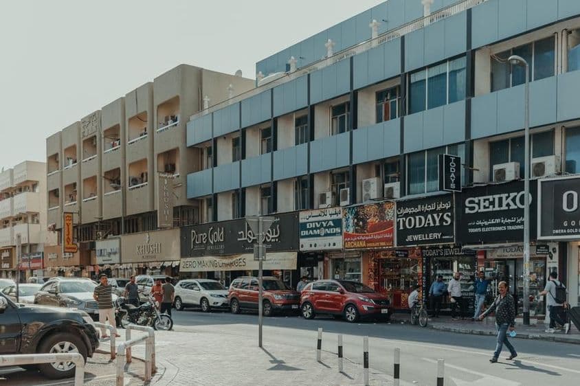 Forgalmas Bur Dubai utca ékszerüzletekkel, gyalogosokkal és autókkal egy napsütéses napon.