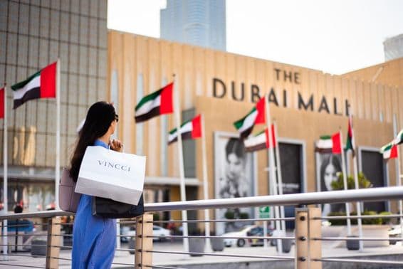 Ázsiai turista bevásárlószatyrokkal a Dubai Mall főbejárata előtt.