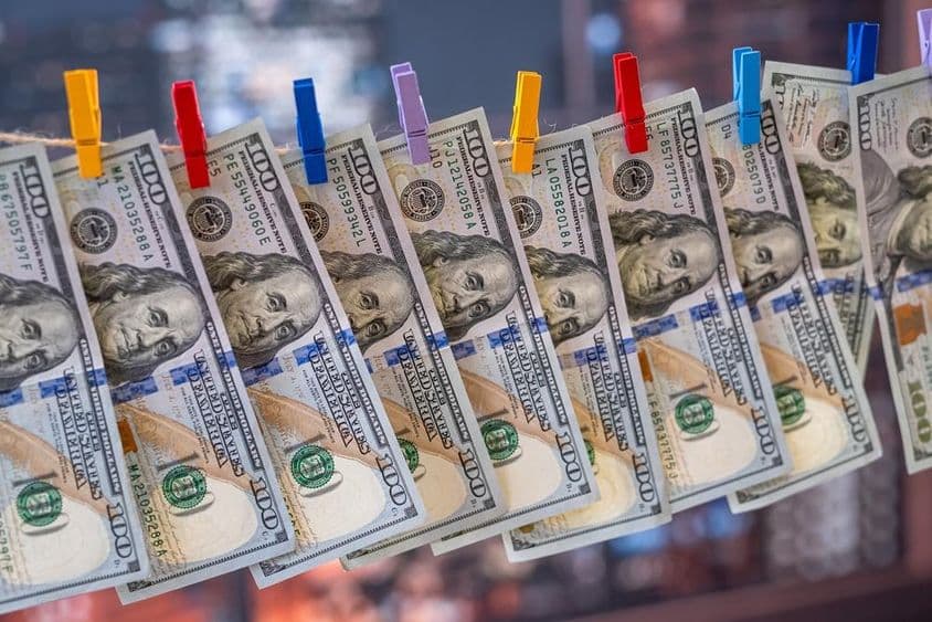 100 új dolláros bankjegy lóg a ruhaszárító kötélen fakapcsokkal.