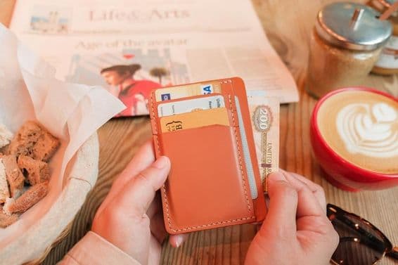 Egy kéz 200 egyesült arab emírségekbeli dirhamot vesz elő egy barna bőr kártyatartóból.