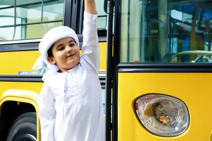 Arab általános iskolás diák egy sárga iskolabusz közelében.